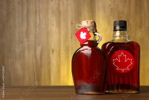 Glass bottles of tasty maple syrup on wooden table. Space for text