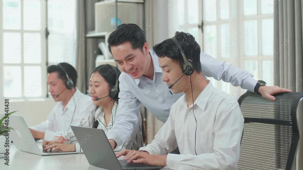 A Man Coming To Help One Man Of Three Asian Call Center Agents In Headsets To Work With Computer While Two Of His Colleagues Are Speaking With Customer At The Office
A Man Coming To Help One Man Of Three Asian Call Center Agents In Headsets To Work With Computer While Two Of His Colleagues Are Speaking With Customer At The Office