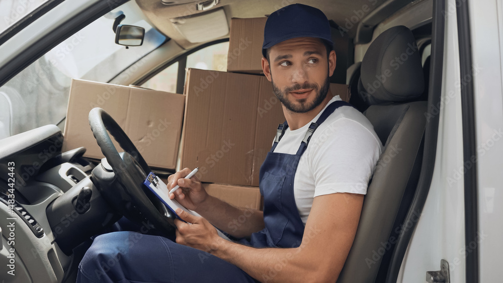 Courier writing on clipboard near carton boxes in car Courier writing on clipboard near carton boxes in car