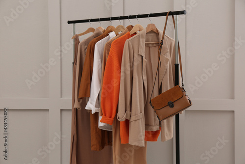 Rack with stylish women's clothes and bag near light wall
