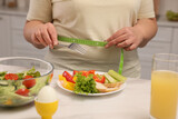 Overweight woman measuring waist while having meal at home, closeup