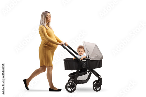 Full length profile shot of a pregnant woman walking and pushing a child in a stroller