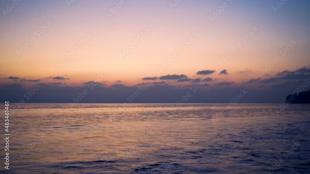 slow panning shot showing the sunset dusk scene with purple pink water lapping waves and the trees and clouds in the distance at havelock andaman island India a perfect vacation spot slow panning shot showing the sunset dusk scene with purple pink water lapping waves and the trees and clouds in the distance at havelock andaman island India a perfect vacation spot