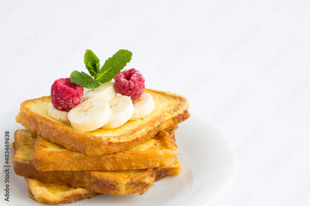 Close-up on french toasts with banana and raspberry on the white plate on the white background. Copy space. Close-up on french toasts with banana and raspberry on the white plate on the white background. Copy space.