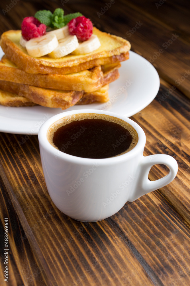 Coffee cup, french toasts with banana and raspberry on the wooden background. Breakfast. Location vertical. Coffee cup, french toasts with banana and raspberry on the wooden background. Breakfast. Location vertical.
