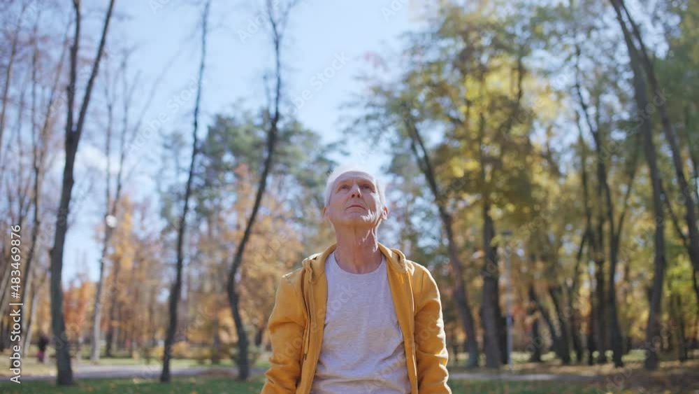 Aged man stretching body, doing breathing exercises in sunny autumn park Aged man stretching body, doing breathing exercises in sunny autumn park