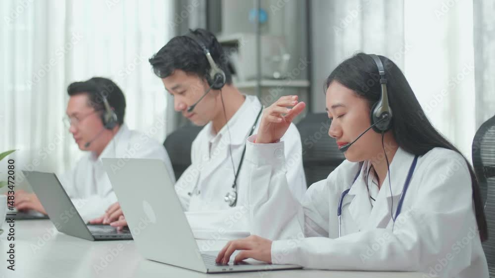 A Woman Of Three Asian Doctors With Stethoscopes In Headsets Working As Call Center Agent Is Tired Due To Working While Her Colleagues Are Speaking And Typing During The Call At The Office
A Woman Of Three Asian Doctors With Stethoscopes In Headsets Working As Call Center Agent Is Tired Due To Working While Her Colleagues Are Speaking And Typing During The Call At The Office