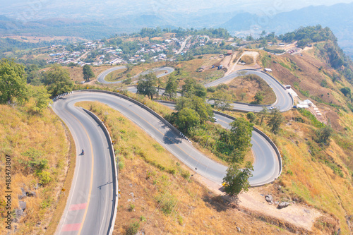 Aerial view of cars driving on curved, zigzag curve road or street on mountain hill with green natural forest trees in rural area of Nan, Thailand. Transportation.