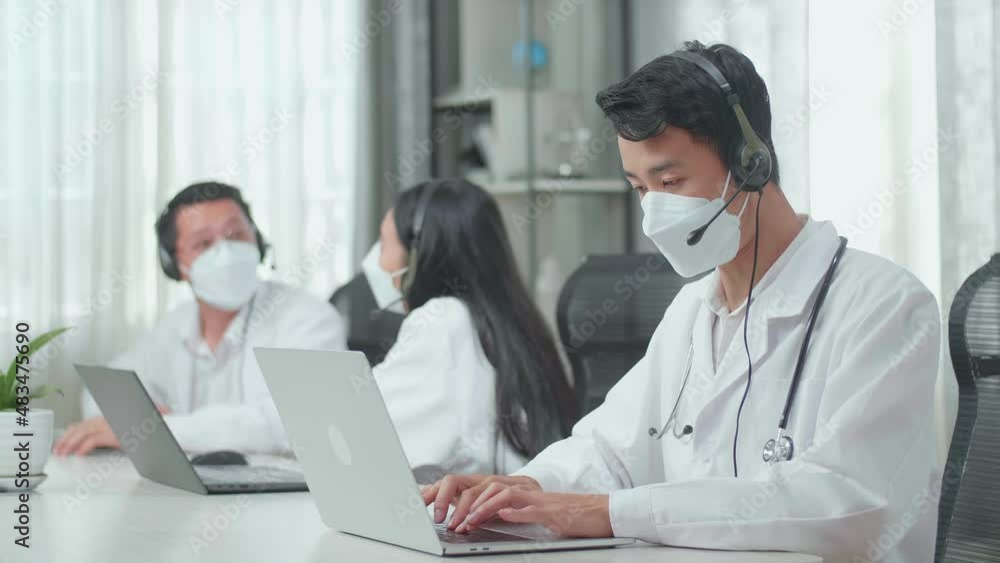 A Man Of Three Asian Doctors With Stethoscope In Headset And Mask Working As Call Center Agents Speaking On The Call And Typing While His Colleagues Are Talking During Working At The Office
A Man Of Three Asian Doctors With Stethoscope In Headset And Mask Working As Call Center Agents Speaking On The Call And Typing While His Colleagues Are Talking During Working At The Office