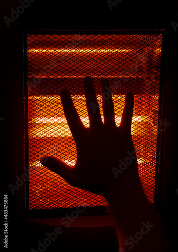 hand in front of an electric heater, inside an apartment in winter.