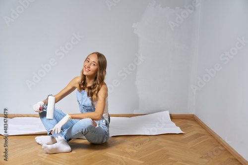 Young cute woman renovate and paint white color wall. Girl in blue denim overall happy to work