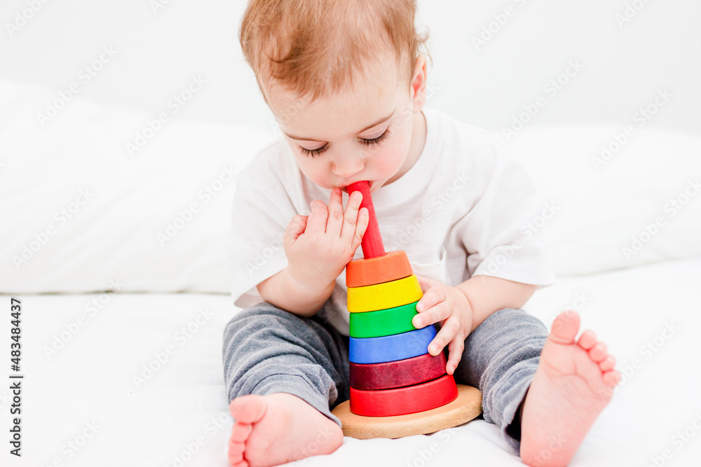 Pretty child 1 years old wearing white tshirt playing with wooden pyramid. Concept of wooden toy, children development Pretty child 1 years old wearing white tshirt playing with wooden pyramid. Concept of wooden toy, children development