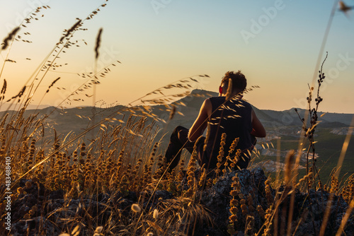 An unrecognizable young boy sitting on rocks and resting with a beatiful scene of a sunset and a mountain in the background