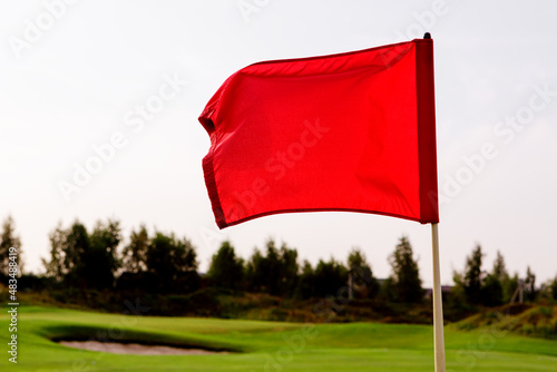 A red flag is fluttering in the wind over the golf course.