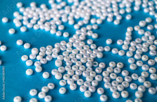 Selective focus, white pearl beads for needlework on a blue background. Making jewelry from beads, embroidery, mosaic and knitting