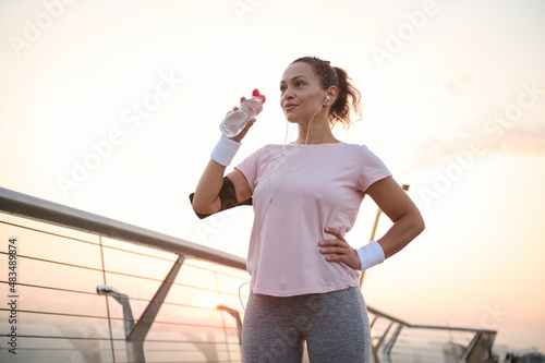 Photos Beautiful sportswoman, female athlete drinks water to hydrate body after outdoor cardio workout