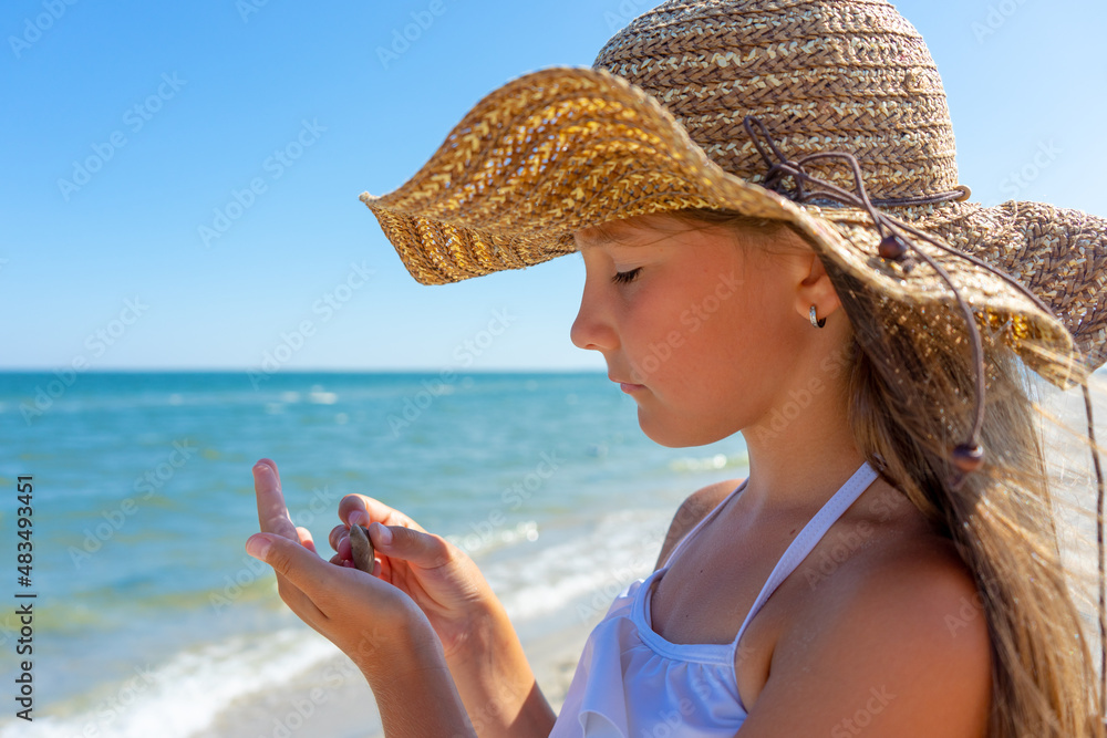 Summer, beautiful little girl in a straw hat is resting on the beach ...