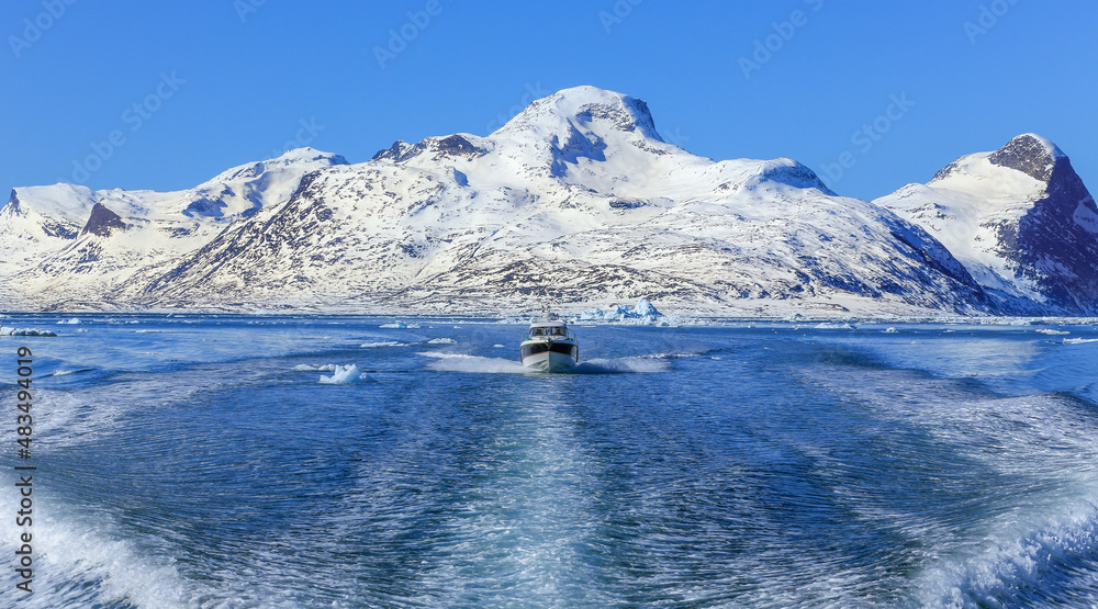 Motor boat in the middle of Nuuk fjord with frozen rocks in the background, Greenland