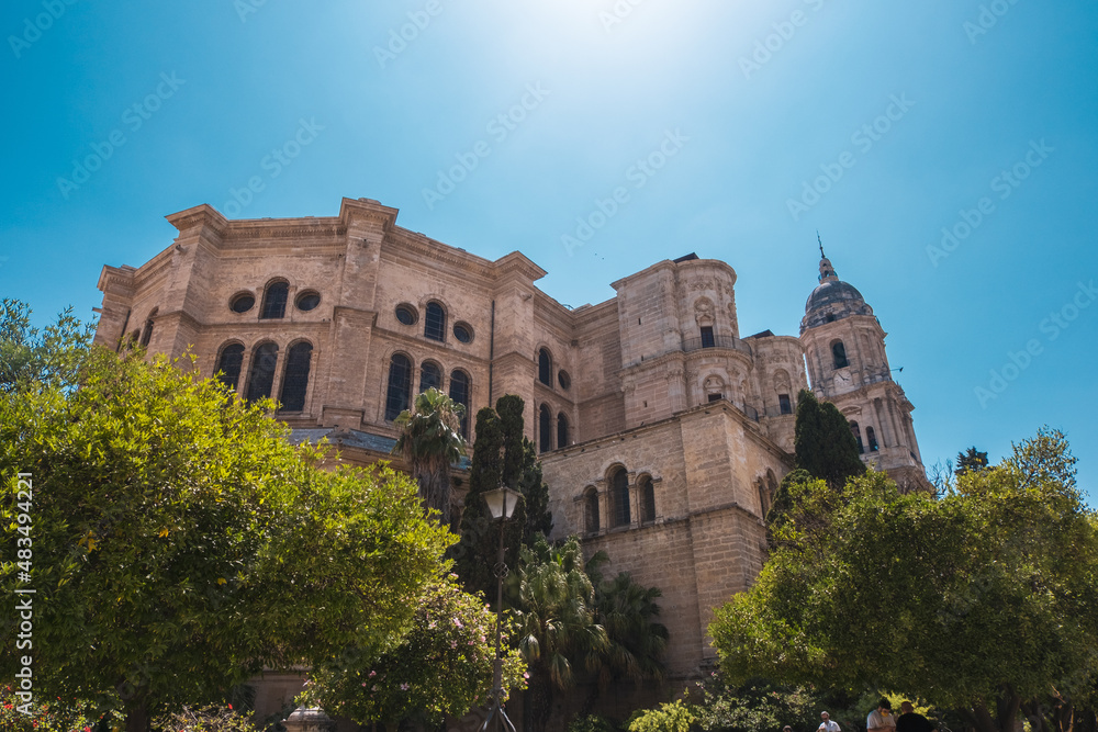 Froschblick auf südeuropäische Kirche mit Bäumen vor klarem, blauem Himmel | Malaga, Spanien