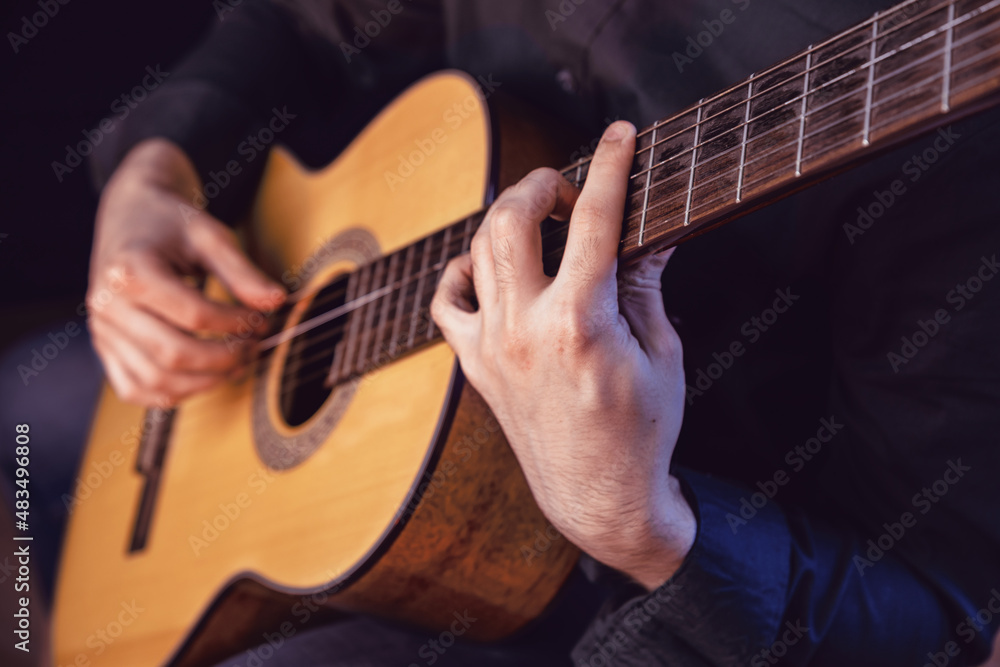 Fototapeta premium The guy in the dark shirt is plucking the strings of a six-string guitar