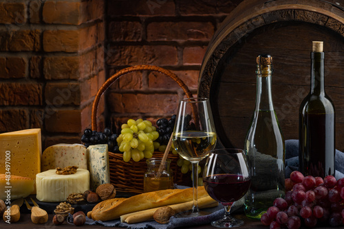 Charcuterie plate board, and wine. Old oak vintage barrel. Cheese pieces, nuts, grapes, honey on a wooden table. Refreshments and tasting alcoholic drinks in the wine cellar