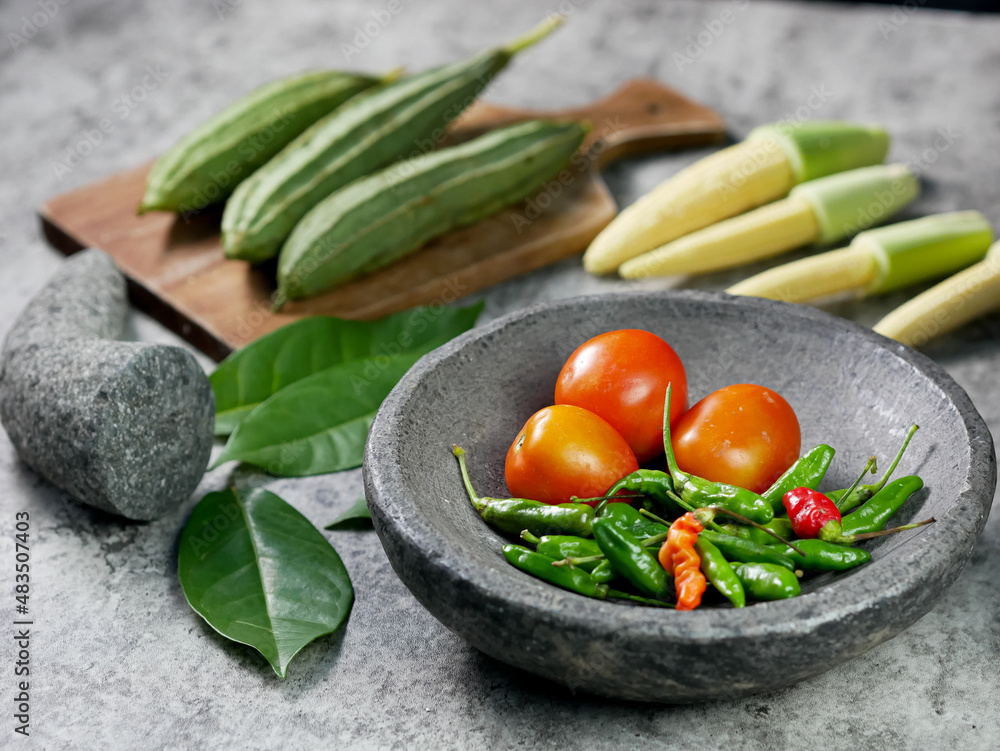 chilies and tomatoes in a mortar, recipe for vegetable baby corn and luffa acutangula with tomato sauce.