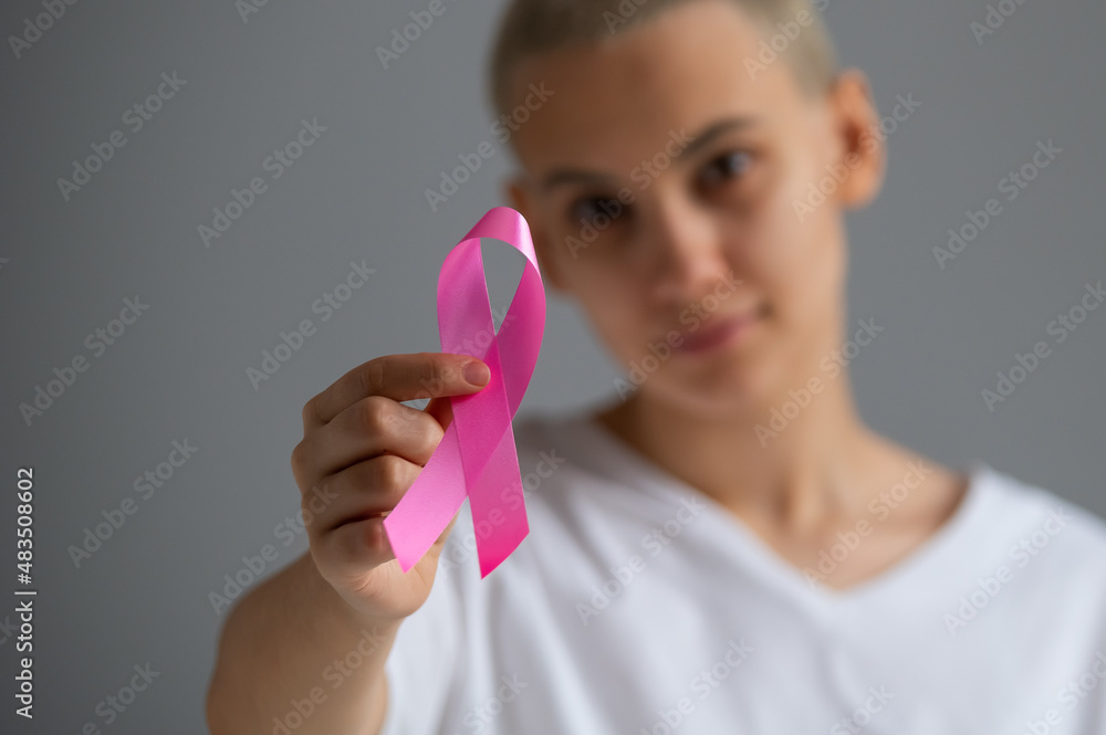 A faceless woman wearing a white t-shirt holds a pink ribbon as a symbol of breast cancer on a white background. A faceless woman wearing a white t-shirt holds a pink ribbon as a symbol of breast cancer on a white background.