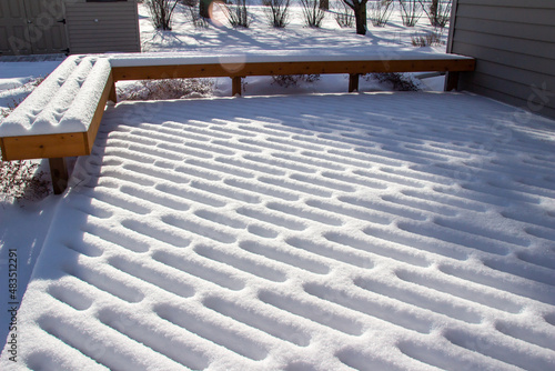 Close up view of fresh snow texture designs on a wooden deck and bench in winter with natural sunlight 
