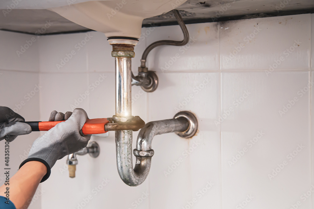 Technician plumber using a wrench to repair a water pipe under the sink. Concept of maintenance, fix water plumbing leaks, replace the kitchen sink drain, cleaning clogged pipes is dirty or rusty. Technician plumber using a wrench to repair a water pipe under the sink. Concept of maintenance, fix water plumbing leaks, replace the kitchen sink drain, cleaning clogged pipes is dirty or rusty.
