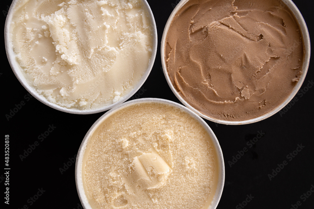 Botes de helado de varios sabores, toma picada, fondo negro. Botes de helado de varios sabores, toma picada, fondo negro.