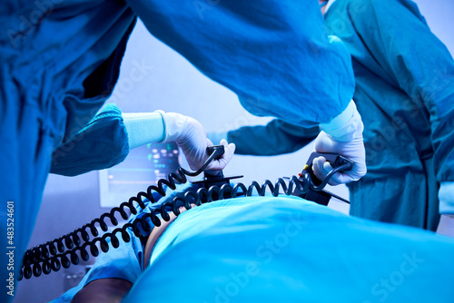 Doctor holding defibrillator paddles in both hands prepare help patient in operating room at hospital photo