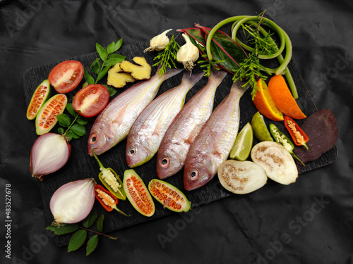 Fresh Pink Perch (thread finned Bream) Decorated with vegetables on a wooden pad,Black Background,Selective focus photo