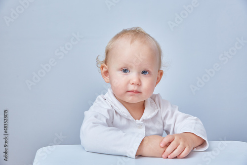 Portrait of a child in light clothes sitting at a table on a light background.