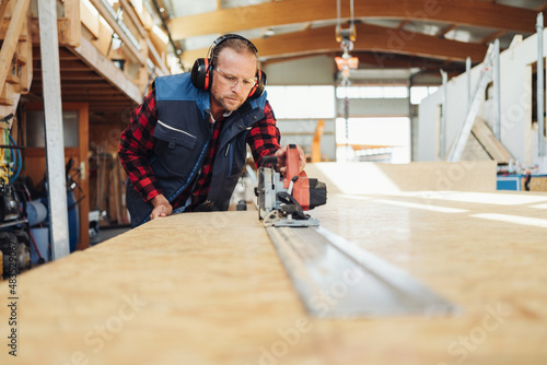 Carpenter or joiner in a woodworking factory cutting timber