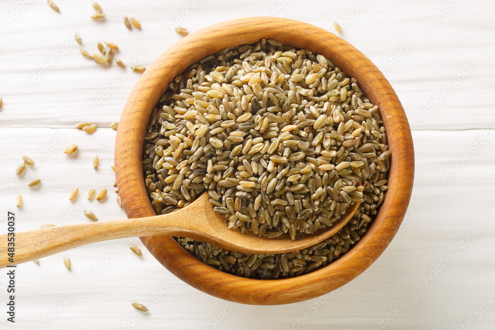 Uncooked, raw freekeh or firik, roasted wheat grain, on wooden plate with wood spoon on white rustic table. Horizontal top view from above Uncooked, raw freekeh or firik, roasted wheat grain, on wooden plate with wood spoon on white rustic table. Horizontal top view from above
