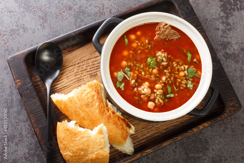 Chorba Frik is a traditional soup made from lamb, cracked wheat, tomatoes, onion, celery, coriander, paprika, parsley close-up in a plate on the table. Horizontal top view from above photo