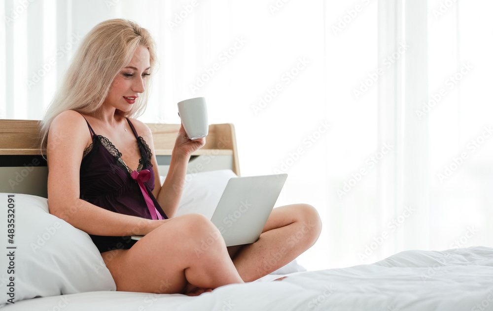 Portrait studio shot Caucasian blonde long hair hot seductive female fashion model in black sexy lingerie underwear sitting smiling holding drinking coffee browsing surfing internet shopping online Portrait studio shot Caucasian blonde long hair hot seductive female fashion model in black sexy lingerie underwear sitting smiling holding drinking coffee browsing surfing internet shopping online