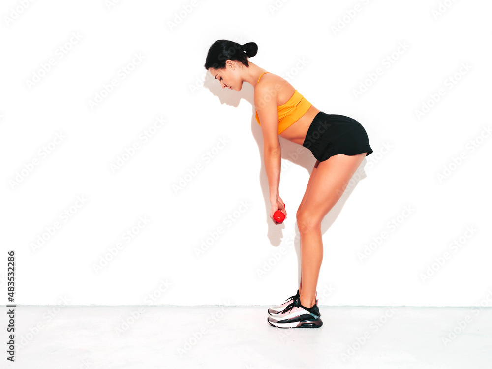 Fitness woman in sexy sports clothing. Young beautiful model with perfect body. Female posing in studio near white wall at summer sunny day. Doing exercises with dumbbells
