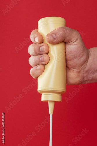 Fotografi Squeezing a mayonnaise bottle isolated on a red background.
