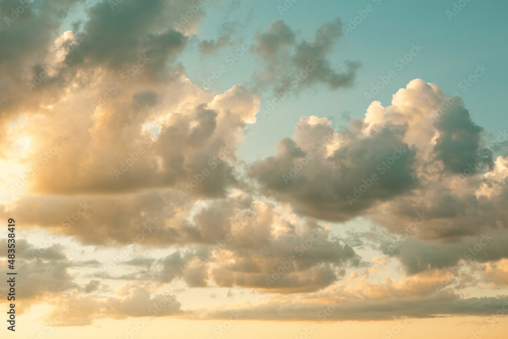 Fototapeta premium Cumulus clouds in the sky at sunset in summer illuminated by the orange light of the sun. Heavenly magic light.