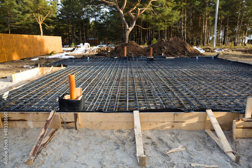 Iron fittings on a wooden formwork with laid pipes are the basis for pouring the foundation of the house with a concrete slab. Construction of cottages, design, engineering communications. photo