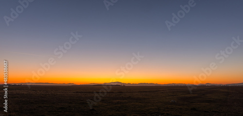 incredible sunset and blue hour over a flat landscape with mountains on the horizon panorama