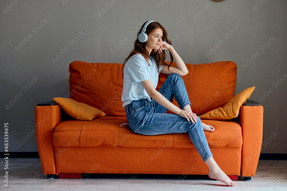 Obraz premium woman on the orange sofa listening to music with headphones technologies