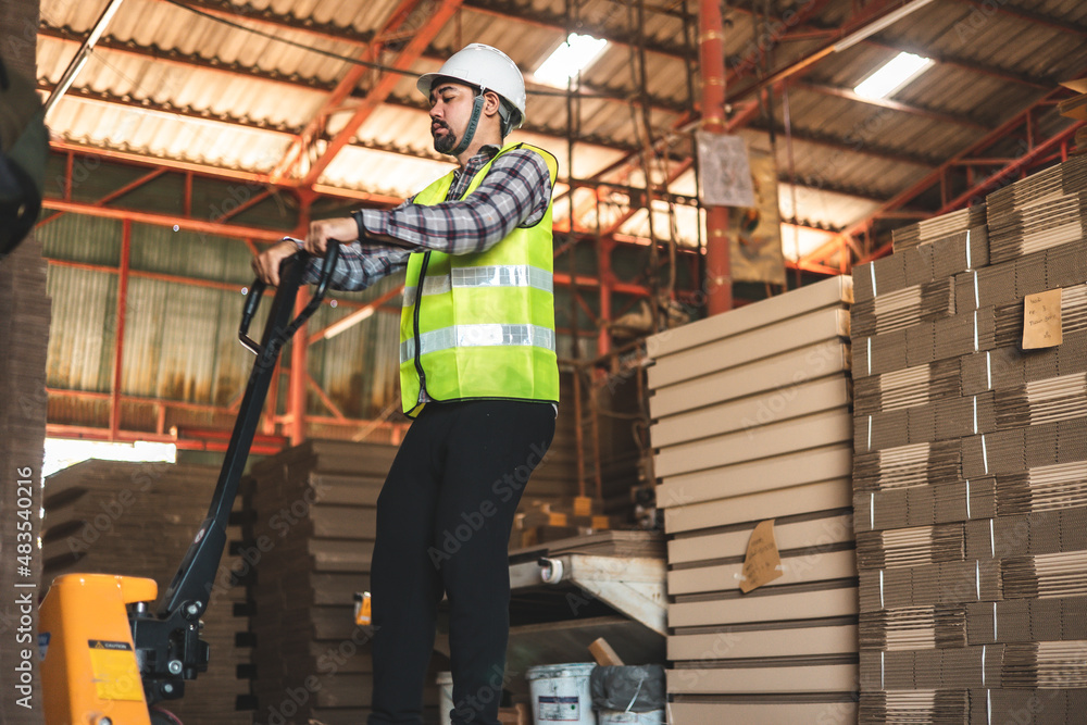 Engineer wearing safety helmet and vest holding clipboard and take note on the paper in the automotive part warehouse.Products and corrugated cardboard. Engineer wearing safety helmet and vest holding clipboard and take note on the paper in the automotive part warehouse.Products and corrugated cardboard.