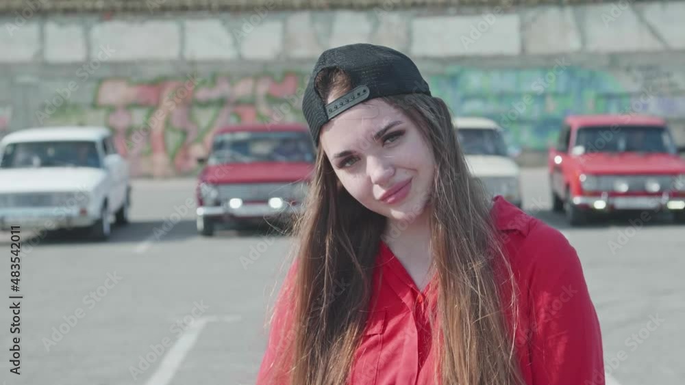 Portrait of a female teenager in a red shirt and baseball cap on a blurred background with antique cars