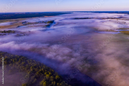 Aerial view of a beautiful summer landscape with a fog while dawn. Photo from drone of a foggy landscape in spring. Top view to land while sunrise. Early morning in nature, misty weather.