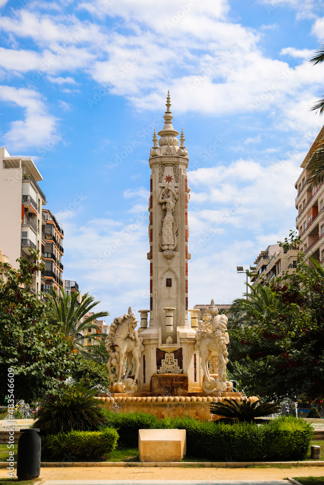 A square in Alicante with some statues in the shape of a horse and with a fountain 
in the middle and buildings behind
