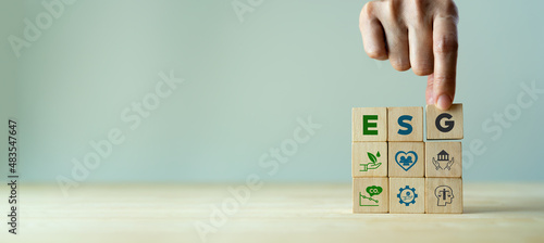 ESG concept of environmental, social and governance. Sustainable corporation development. Hand holds wooden cubes with abbreviation ESG standing with other ESG icons on grey background. Copy space.