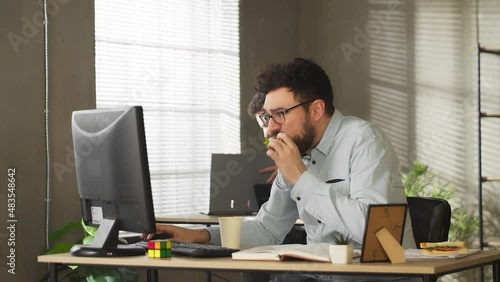 Busy casual young businessman eating lunch sandwich food at office desk writing