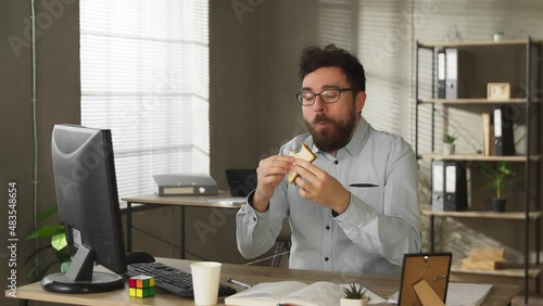 Busy casual young businessman eating lunch sandwich food at office desk writing